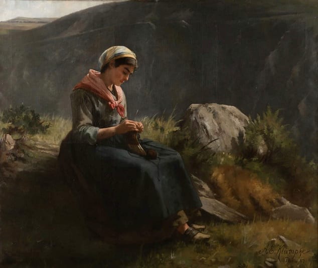 A seated woman in scarf and headwrap sits outdoors knitting among mountain scenery.