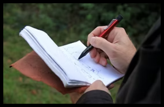 The hands of an artist, holding a sketchbook and pen, outdoors